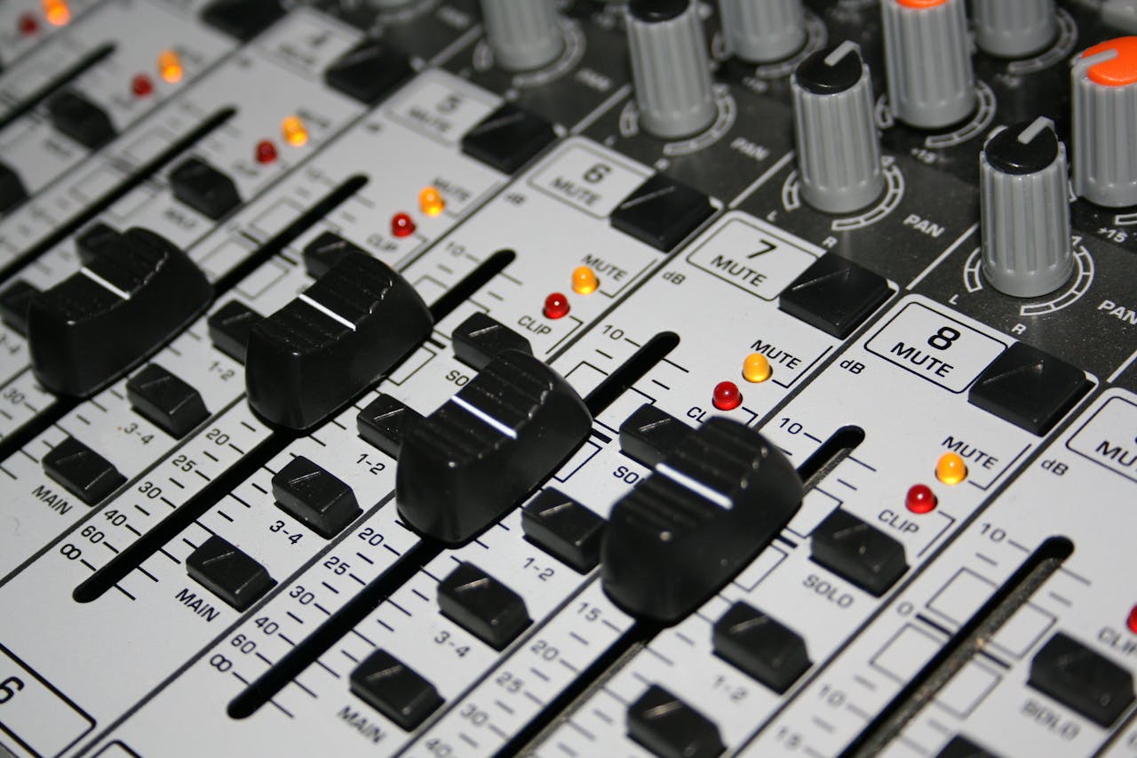 Detailed shot of a professional audio mixer with knobs and sliders illuminated by indicator lights.